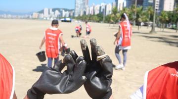 pessoas seguram bitucas e ao fundo outras limpam a praia #paratodosverem