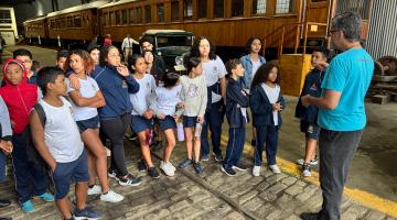 alunos ouvindo uma pessoa em pé #paratodosverem