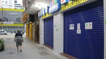 Portas de lojas de rua fechadas. Na calçada anda um homem. #Paratodosverem