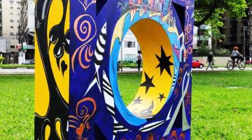 Escultura no jardim, em formato de mureta dos canais, colorida nas cores azul, amarelo e preto. #paratodosverem