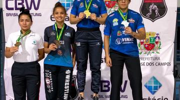 Pódio com as quatro primeiras colocadas segurando as medalhas penduradas em seus pescoços. #pratodosverem