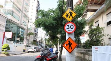 poste com três placas. Uma indica trânsito de crianças, outra a velocidade em 30 km/h e mais uma, indicando a presença de homens trabalhando. #paratodosverem