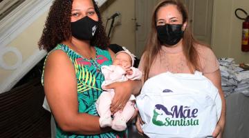 MULHER COM BEBE NO COLO ESTÁ AO LADO DE OUTRA QUE SEGURA UMA BOLSA COM KIT PARA MÃE E BEBE. #PARATODOSVEREM