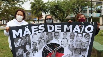 Mulheres mostram bandeira escrito mães de maio e com rostos de vitimas. #paratodosverem