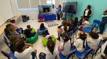 crianças estão sentadas em sala assistindo a um teatro de fantoches. #paratodosverem 