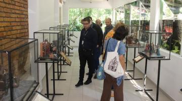 visitantes dentro de sala observando caixas de vidro onde estão as maquetes. #paratodosverem