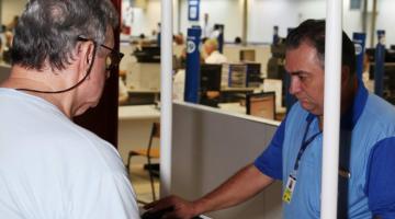 Estande da CET montado em uma área coberta. Um homem está pedindo informações ao outro que usa uniforme da empresa. #Pracegover