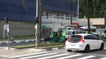 Semáforo em funcionamento em via. Há dois carros passando na pista sobre uma faixa de pedestres. #Pracegover