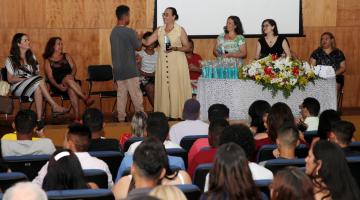 Auditório lotado. Ao fundo, o palco tem uma mesa principal ocupada por mulheres. Uma delas está em pé cumprimentando um homem. #Pracegover