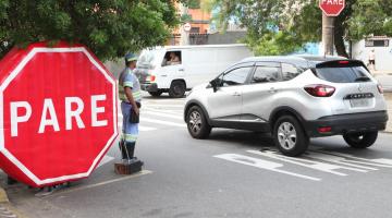 grande inflável onde se lê pare e agente de trânsito ao lado. Carros passam pela rua. #paratodosverem 