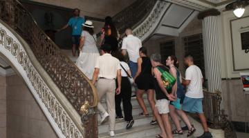 grupo de pessoas sobe escadaria em mármore e corrimãos dourados. #paratodosverem
