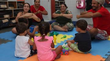 crianças e adultos estão sentados brincando e interagindo. #paratodosverem 