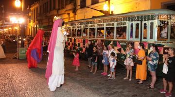 personagens vestidos para interpretar presépio se apresentam diante de bonde cheio de passageiros. #paratodosverem