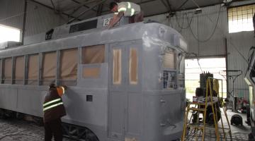 HOmens trabalham na parte externa do veículo. O carro está em uma garagem.