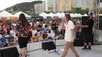 conjunto de três músicos em palco se apresentando para o público ao fundo. #paratodosverem