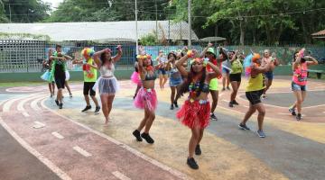 mulheres com roupas coloridas e fantasias dançam em uma quadra. #paratodosverem