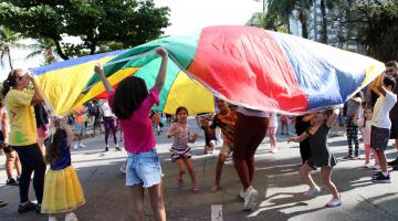 crianças brincam sob lona multicolorida. #paratodosverem