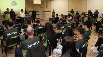 Atletas estão sentados em auditório. #paratodosverem