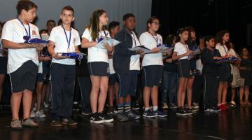 alunos premiados com medalhas e diplomas no palco #pracegover 