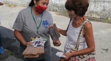 mulher usando máscara entrega folheto e saquinho de papel