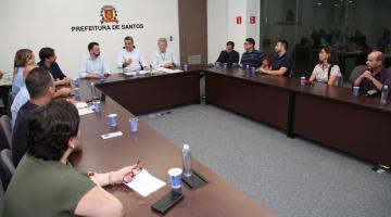 várias pessoas sentadas em sala com mesas dispostas em formato de letra U. #paratodosverem