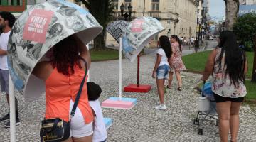 Estruturas e formato de orelhão estão dispostas em praça. Pessoas estão próximas acessando. #Pracegover