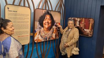 mulheres à frente de paineis de fotos sobre pesca. #paratodosverem