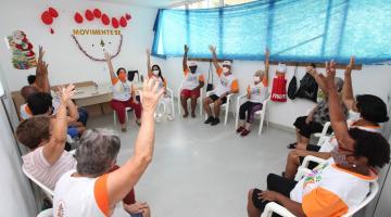 idosos sentados em circulo levantam a mão #paratodosverem