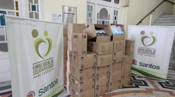 várias caixas de papelão empilhadas em uma sala e ladeadas por banners do Fundo Social de Solidariedade. #paratodosverem