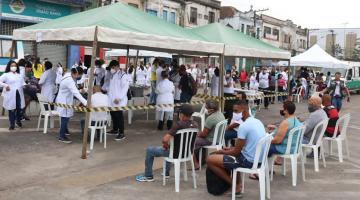 tendas montadas na rua e pessoas sentadas aguardando atendimento.#paratodosverem