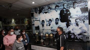 Homem mostra foto de time do Santos e troféus para visitantes #paratodosverem