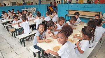 crianças sentadas comendo merenda escolar #paratodosverem