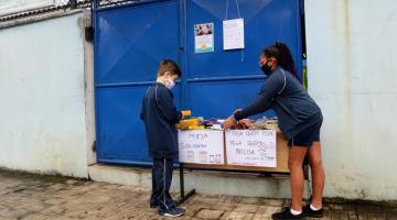 dois alunos estão arrumando pacotes de alimentos sobre uma mesa. #paratodosverem