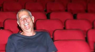 Alcides Mesquita sentado na plateia de um teatro sozinho. #Paratodosverem