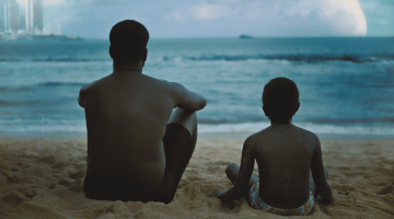 pai e filho olham para o mar em cena de filme #paratodosverem