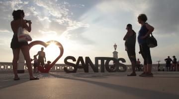 Monumento com a inscrição Santos e coração estilizado ao lado com pessoas olhando e tirando foto. #pracegover