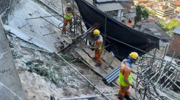 homens estão trabahando em encosta em meio a estruturas de ferro. Há moradias abaixo. #paratodosverem