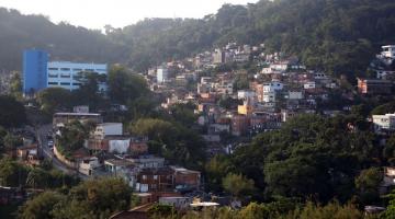 vista geral do morro com casas e uma edificação principal que é uma escola, à esquerda. #paratodosverem