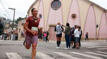 mulher corre e passa sobre faixa de pedestres. Ao fundo, uma igreja. #paratodosverem