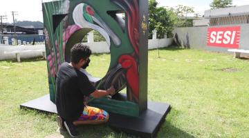 Artista grafita mureta já em finalização. Monumento tem uma grande ave. #paratodosverem