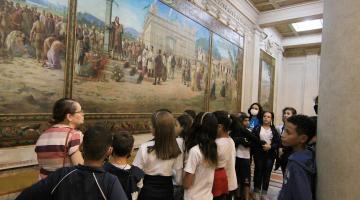 Crianças observam quadro no Museu do Café que retrata a fundação da Vila de Santos. #paratodosverem