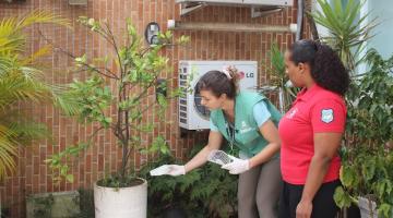 agente está curvada diante de vaso de planta com uma mulher ao lado. #paratodosverem