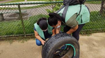 Duas mulheres vistoriam parte interna de pneu em local aberto. #Paratodosverem