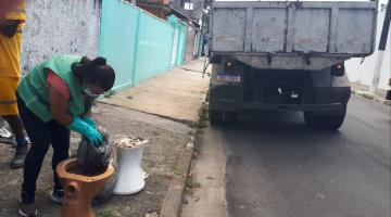 Agente de combate à dengue uniformizada e usando luva mexe em saco dentro de vaso sanitário deixado na rua. #paratodosverem