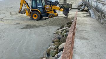 trator leva areia para trecho de ponta da praia. Enrocamento em primeiro plano. #paratodosverem