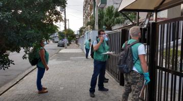 Agentes uniformizados estão na calçada, na entrada de um prédio. #Paratodosverem