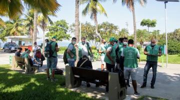 agentes uniformizados estão concentrados no jardim da orla. Em primeiro plano se vê o gramado. Há palmeiras ao redor. #paratodosverem