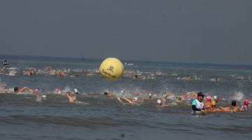 atletas nadando no mar. Ao fundo uma boia grande onde se lê 'Santos'. #paratodosverem