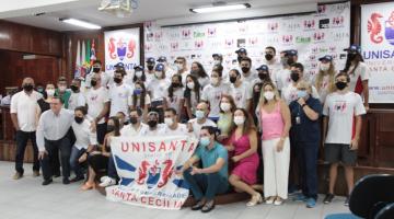 Atletas da natação seguram bandeira da Unisanta ao lado de autoridades esportivas. #pratodosverem 