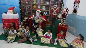 crianças segurando brinquedos e papai noel ao fundo com duas crianças no colo #paratodosverem